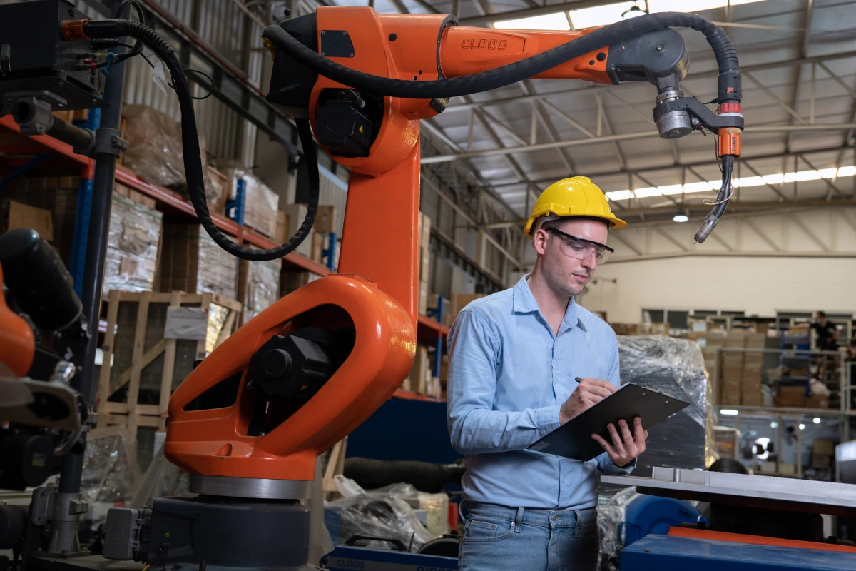 Ingenieur in einer Fabrik, der an der Programmierung eines Schweißroboterarms arbeitet